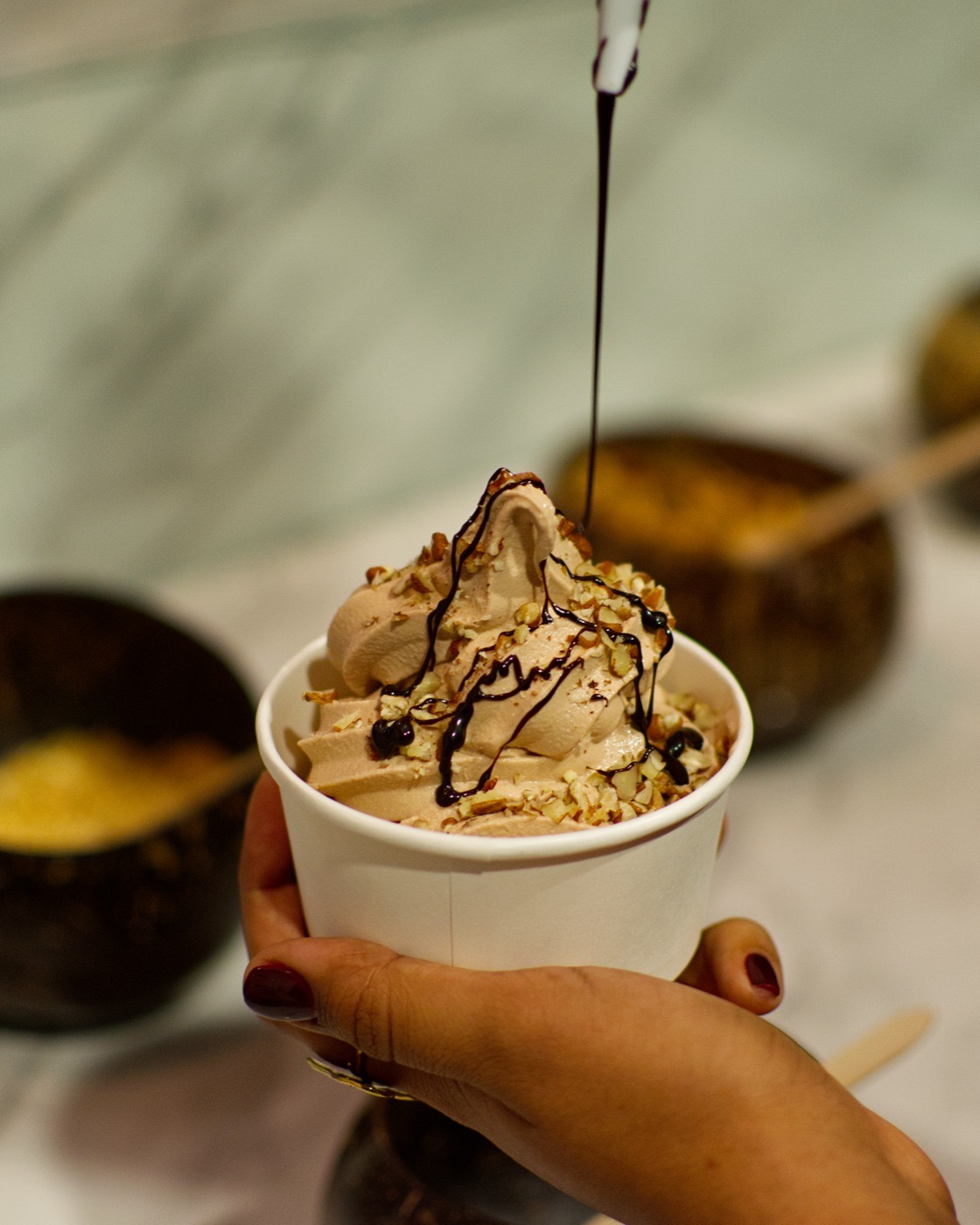 Vaso de helado suave sabor chocolate de nube con trocitos de nuez y salsa de chocolate