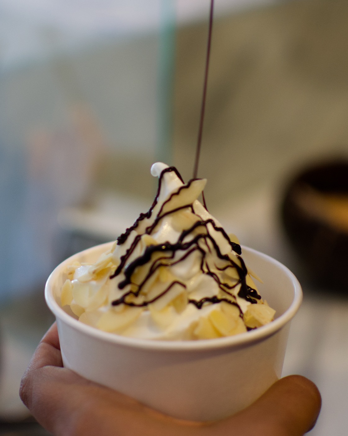 Vaso de helado suave sabor yogurt de nube con almendra fileteada y salsa de chocolate cayendo en hilo