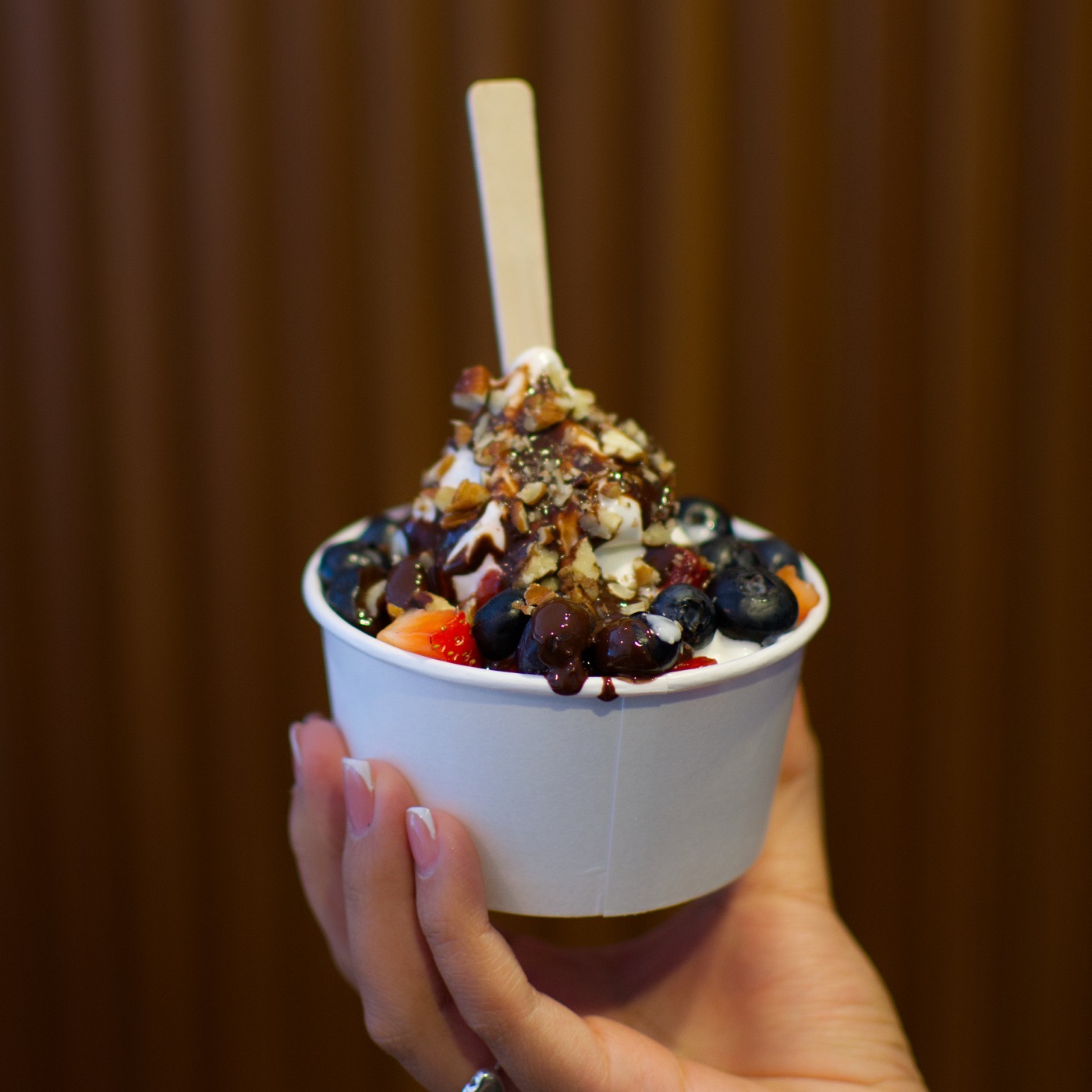 Vaso de helado suave sabor yogurt de nube con arándano, fresa y trocitos de nuez, sostenido en la mano