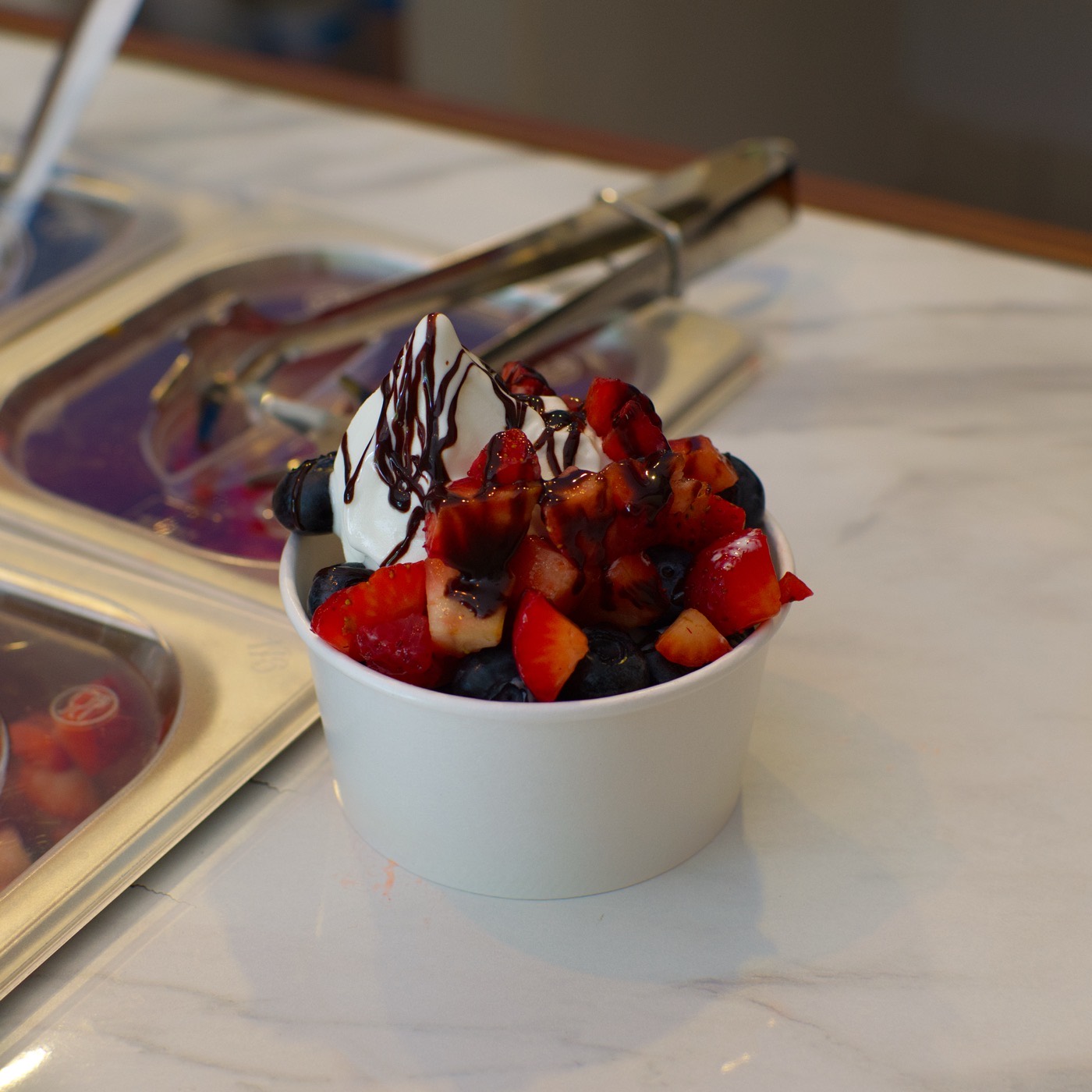 Vaso de helado suave sabor yogurt de nube con fresa, durazno y arándano, servido en el mostrador