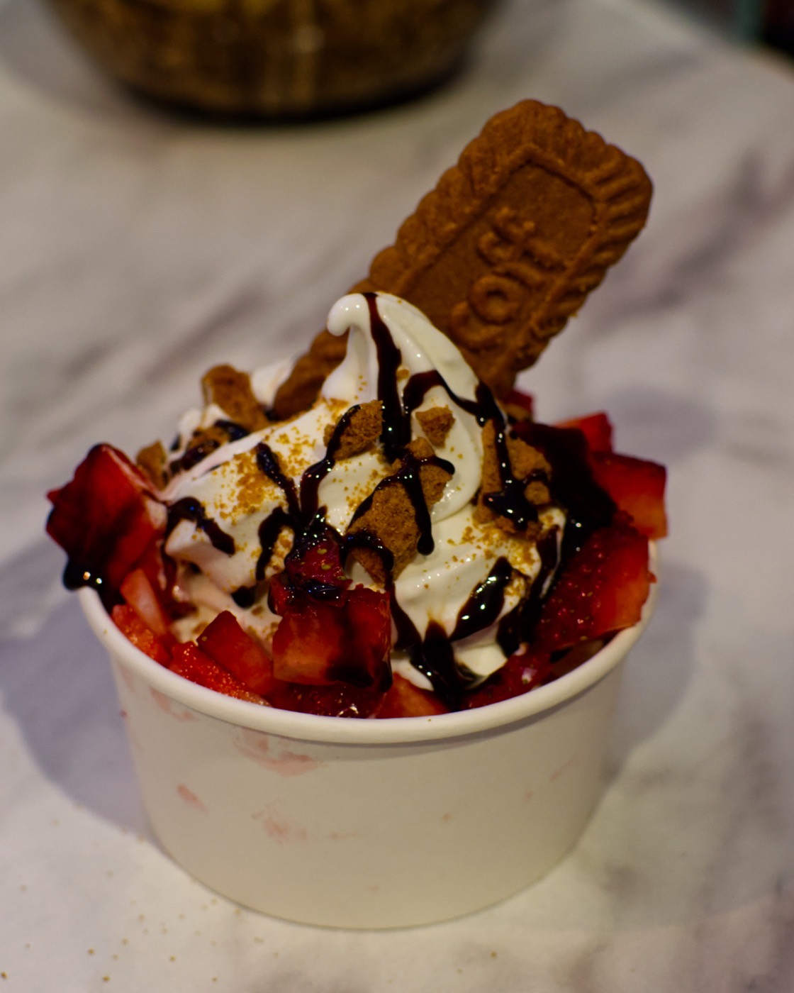 Vaso de helado suave sabor yogurt de nube con fresa picada, galleta Lotus y salsa de chocolate